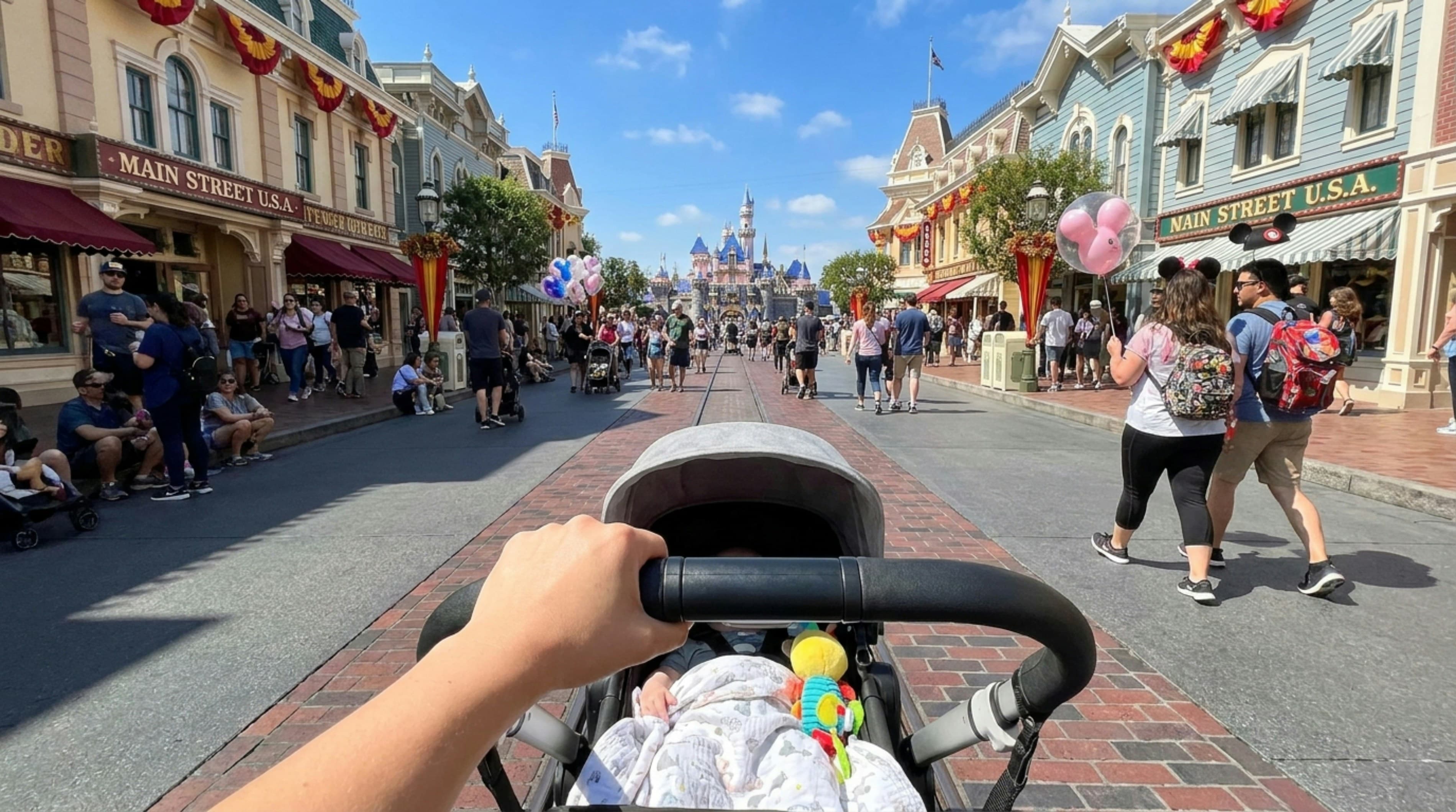 Parent pushing a baby stroller down Main Street at a bustling theme park toward the castle