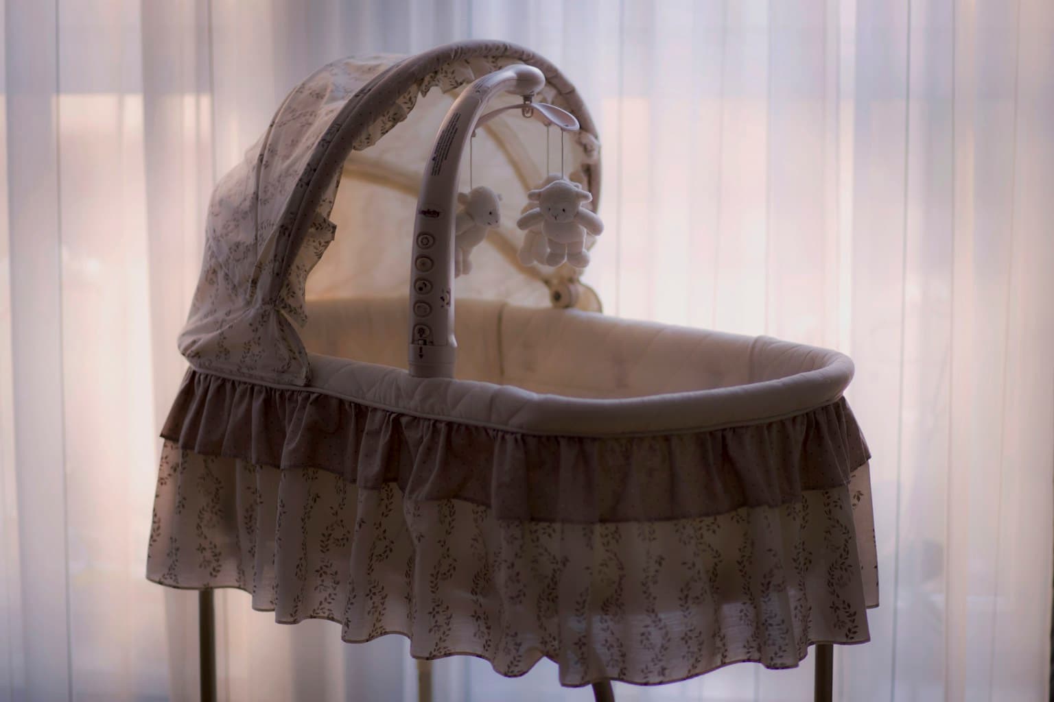 White and black bassinet with a teddy bear mobile in a bright nursery